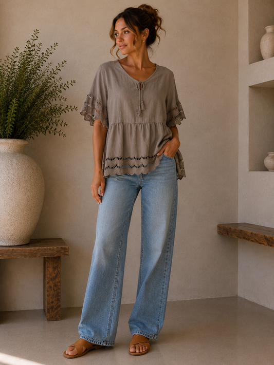 Woman wearing a gray blouse and blue jeans standing in a room with a plant and shelves.