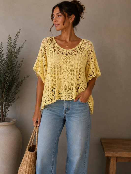 Woman wearing a yellow crochet top and blue jeans, standing against a neutral wall with a plant and wooden table.