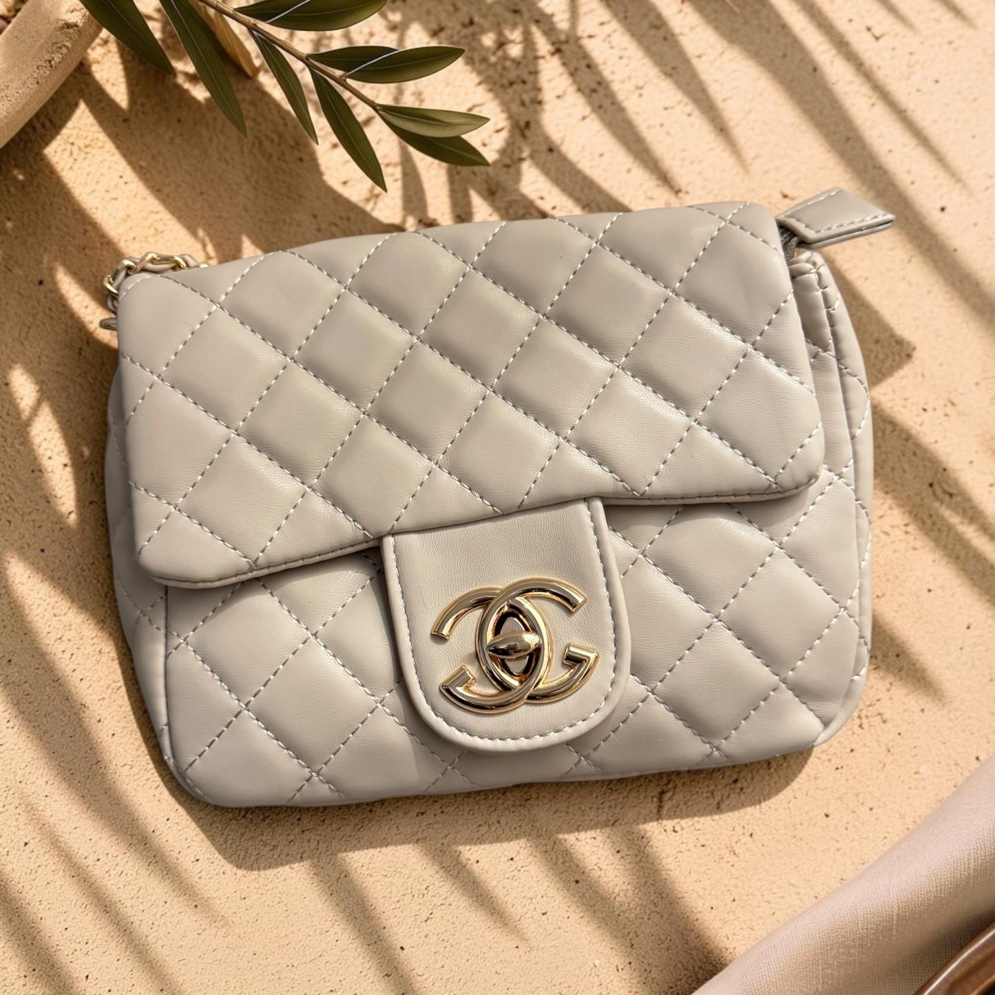 Quilted beige handbag with gold clasp on a sandy background