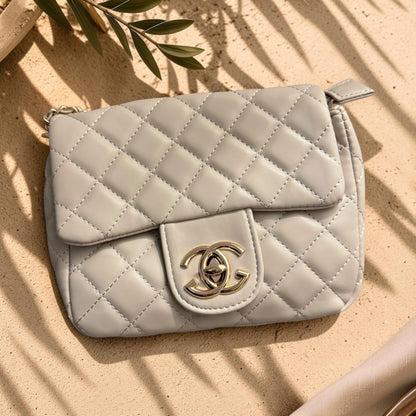 Quilted beige handbag with gold clasp on a sandy background