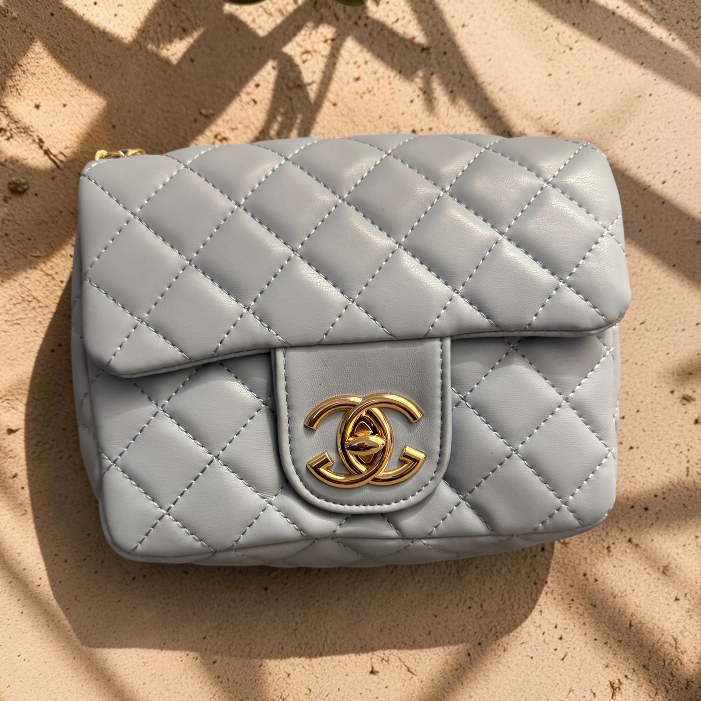 Quilted gray handbag with gold cc logo on a beige surface