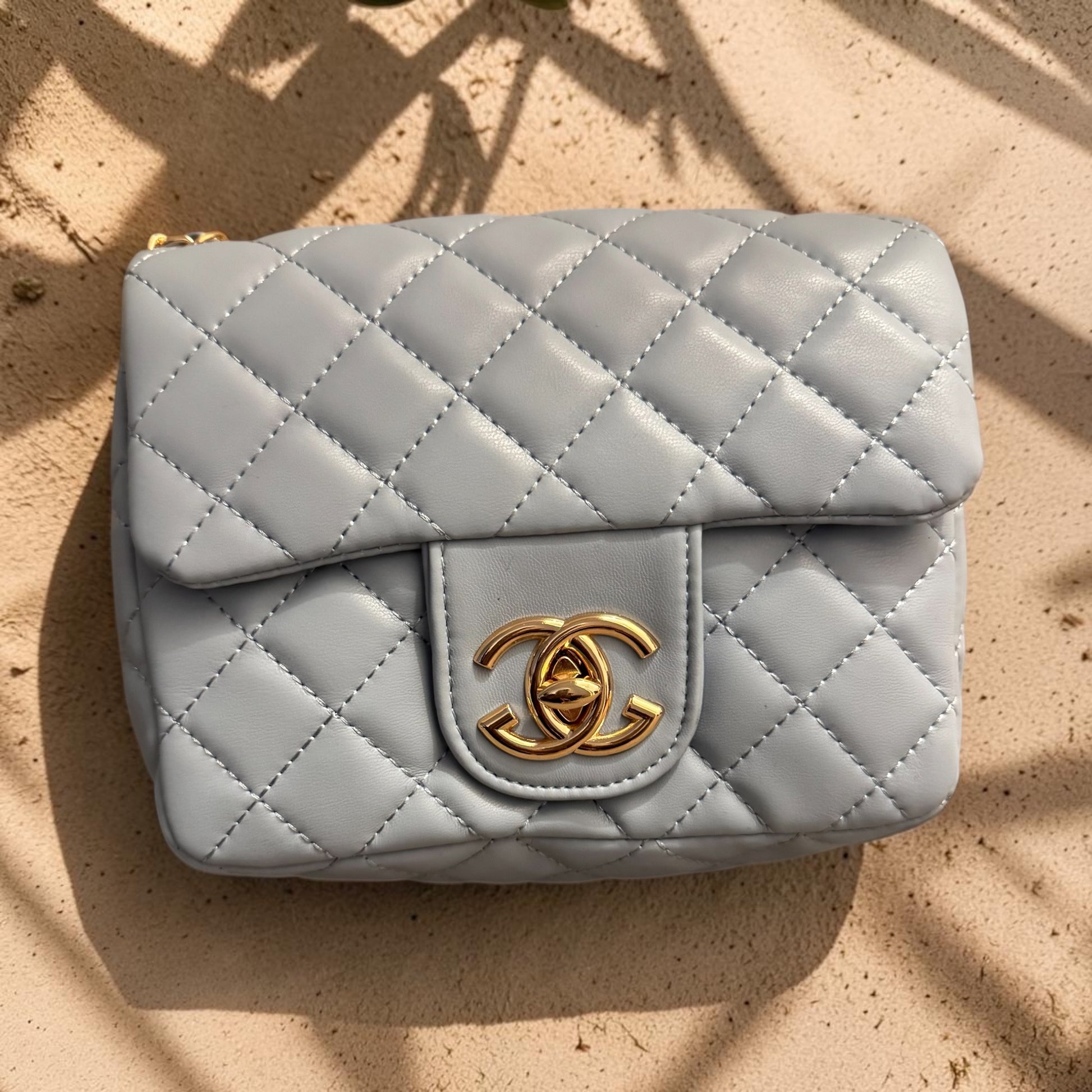 Quilted gray handbag with gold cc logo on a beige surface