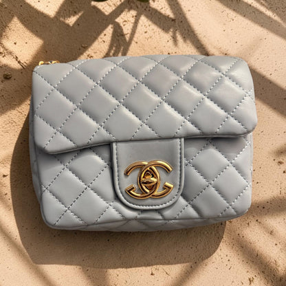 Quilted gray handbag with gold cc logo on a beige surface