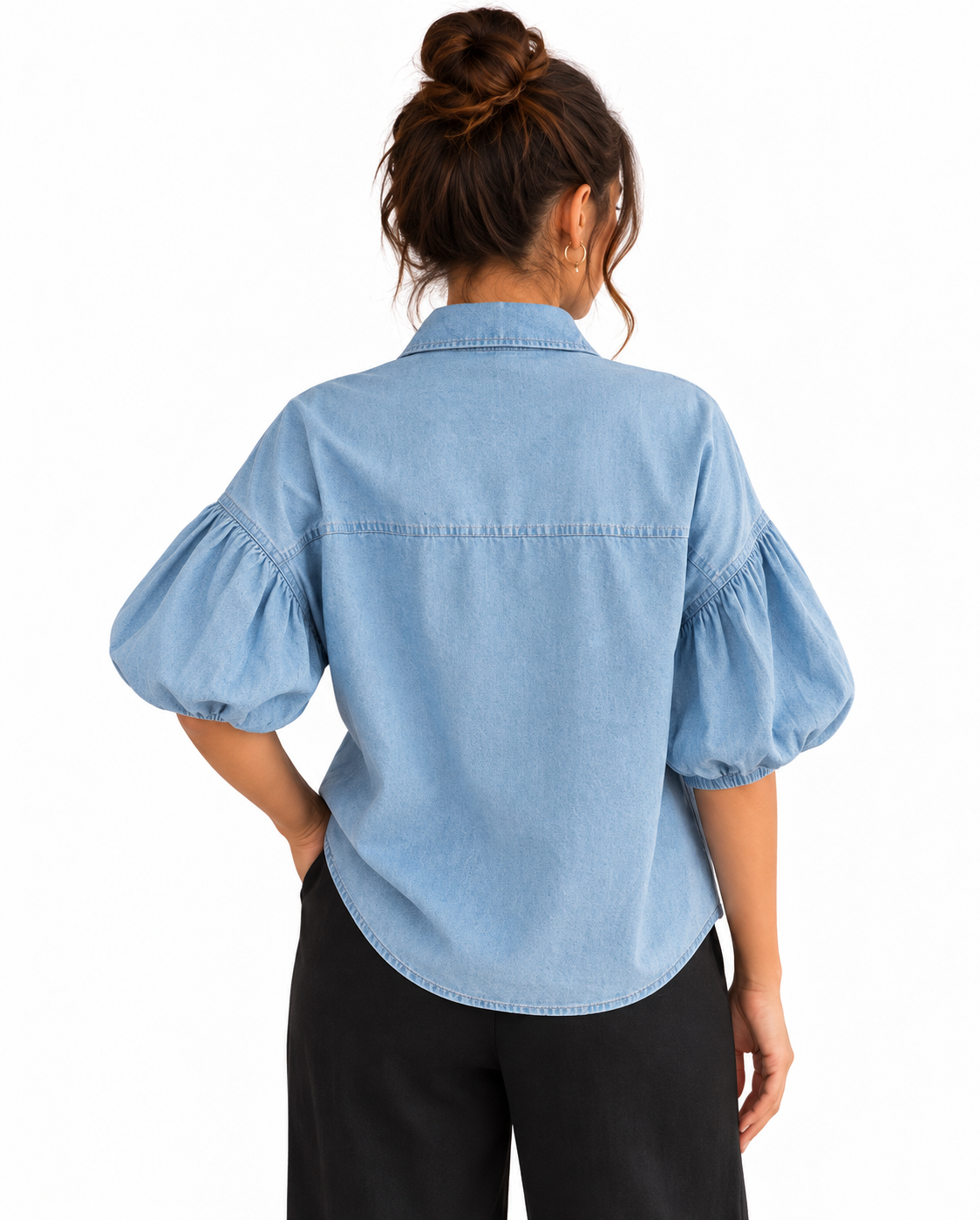 A woman shown from the back wearing a light blue chambray button-up shirt with puffed elbow-length sleeves and black pants, against a plain white background.