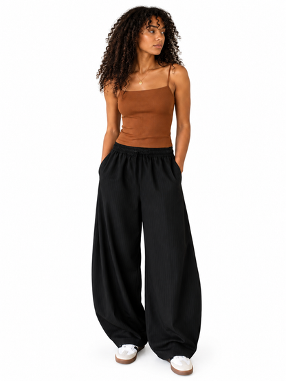 A woman modeling black wide-leg pants with a brown strapless top, standing against a plain white background.