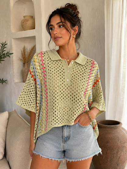A woman models a light sage green crochet knit polo shirt with colorful vertical stripes in pink, blue, orange, and yellow, paired with light-wash denim shorts in a bright, modern room.