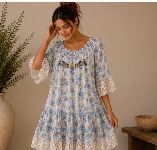 Woman wearing a floral dress standing in a room with a plant and wooden table.