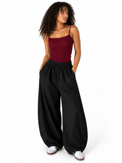 A woman modeling a burgundy spaghetti-strap camisole top and black wide-leg sweatpants against a plain white background.
